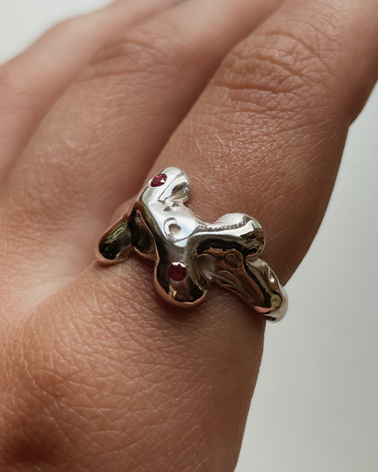 Silver ring with a unique design on a finger against a neutral background