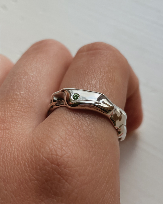 Silver ring with a green stone on a finger against a white background