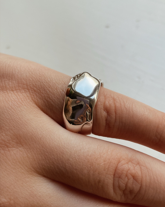 Silver ring on a finger against a neutral background