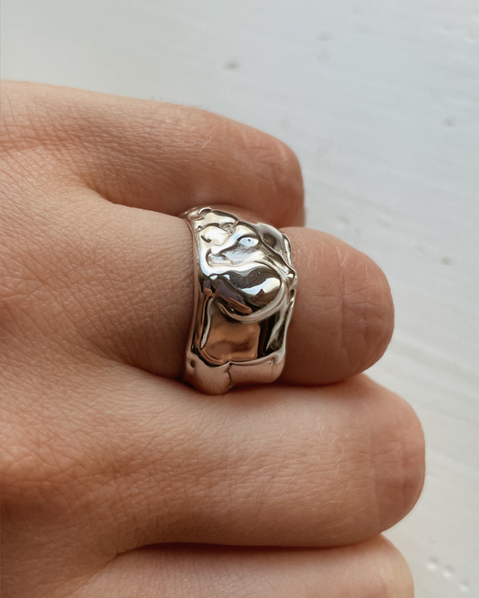 Silver ring on a finger against a neutral background
