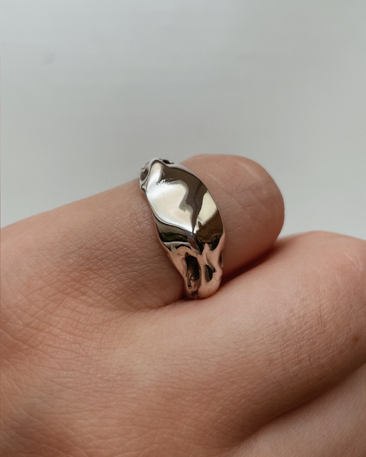 Silver ring on a finger against a neutral background