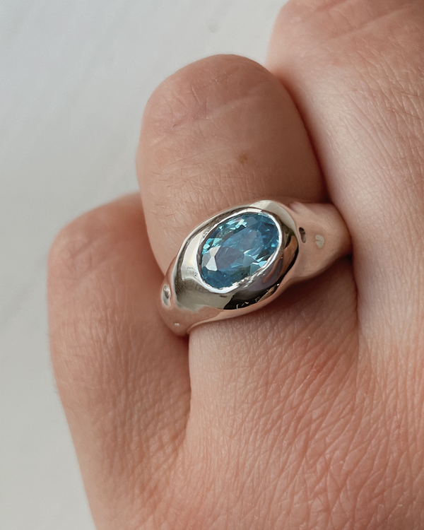 Silver ring with a blue stone on a finger against a plain background