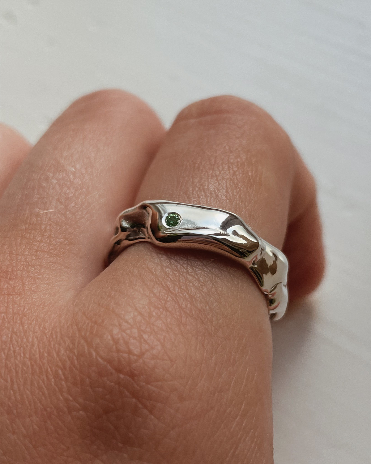 Silver ring with a green stone on a finger against a white background