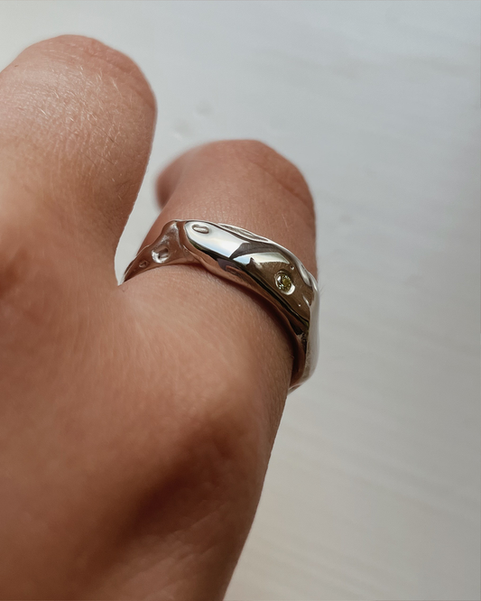 Silver ring with a stone on a finger against a plain background