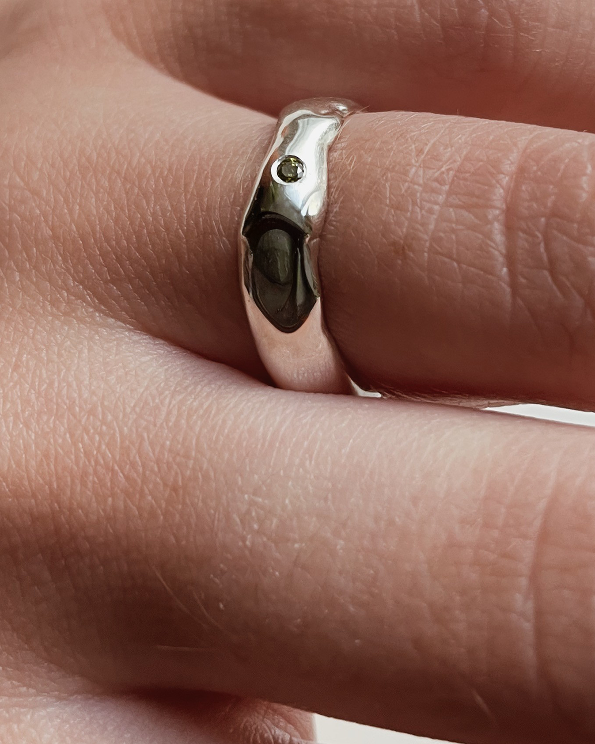 Silver ring with a small green stone on a finger