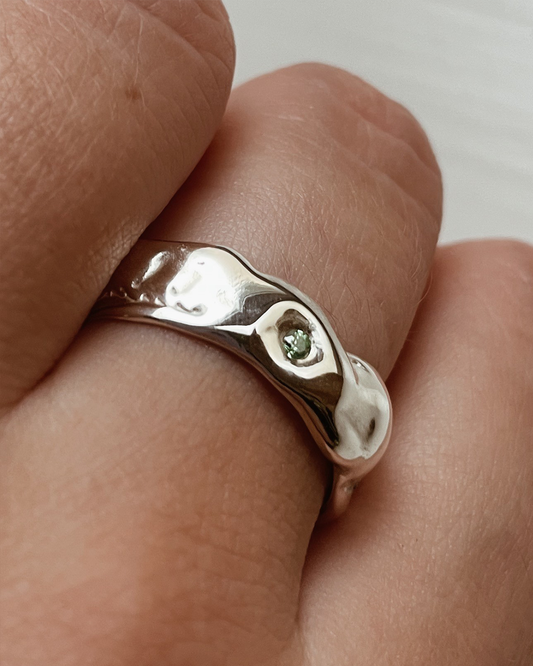 Silver ring with a green stone on a finger against a neutral background
