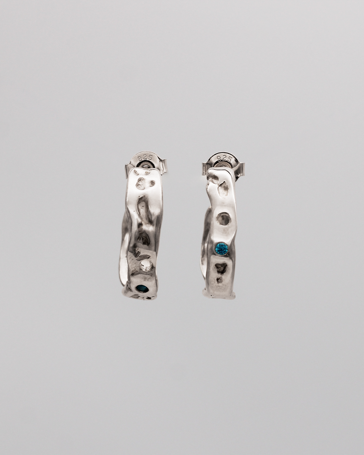 Pair of silver hoop earrings with stones on a gray background