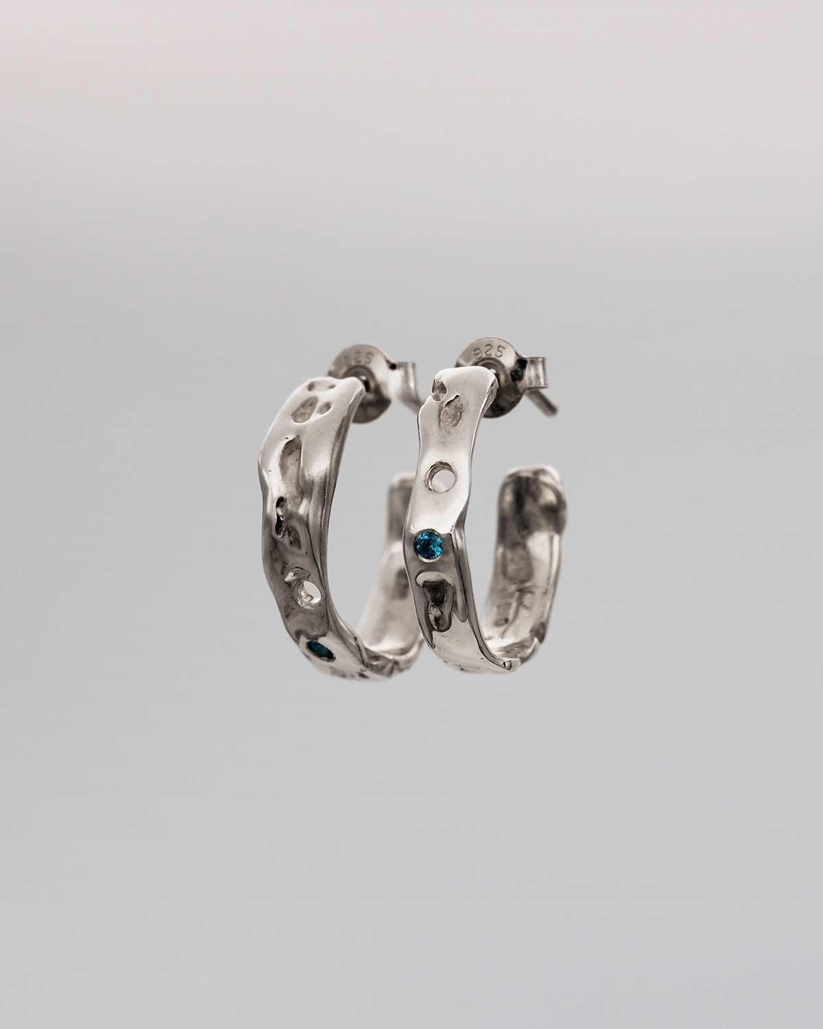 Pair of silver hoop earrings with blue stones on a gray background