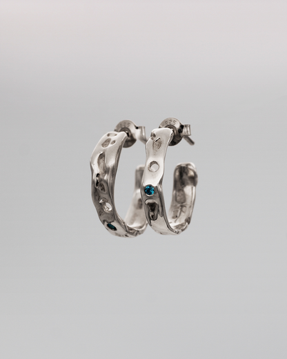 Pair of silver hoop earrings with blue stones on a gray background