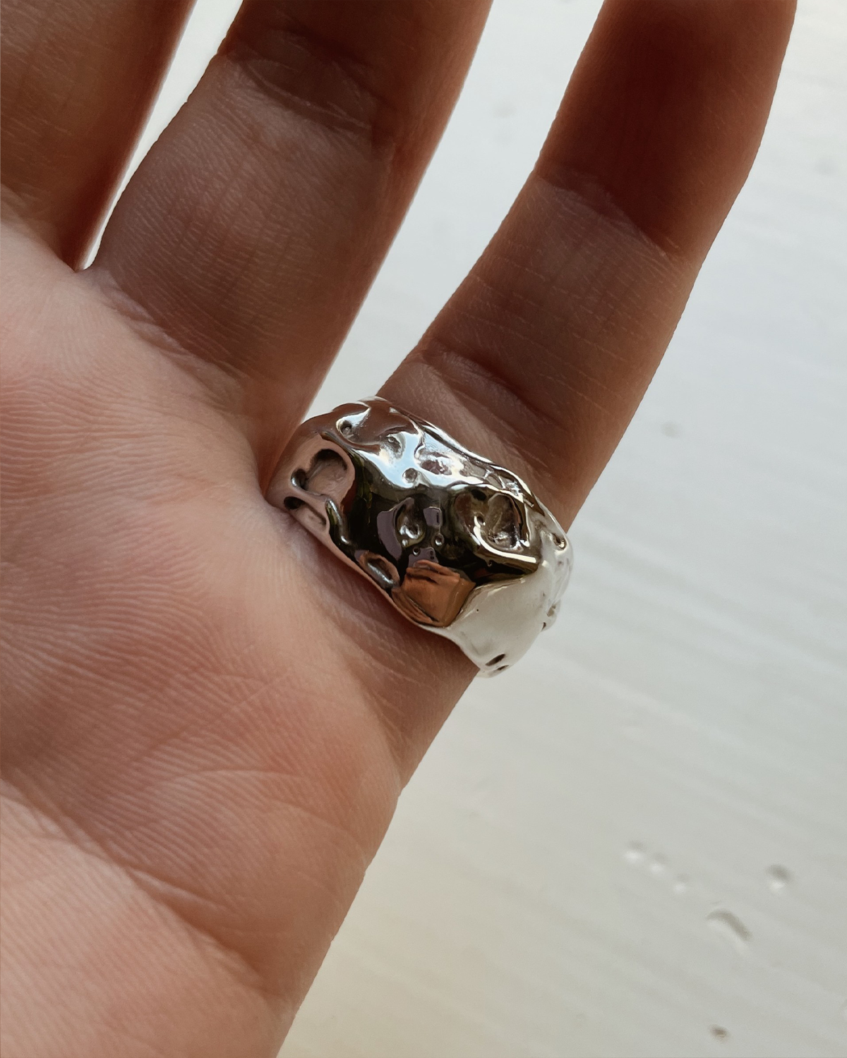 Silver ring with a textured design on a finger against a neutral background