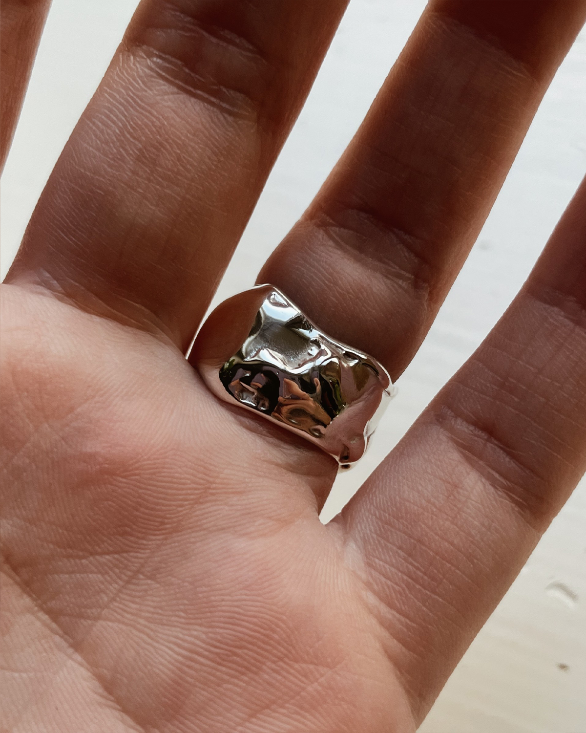Silver ring on a finger with a plain background