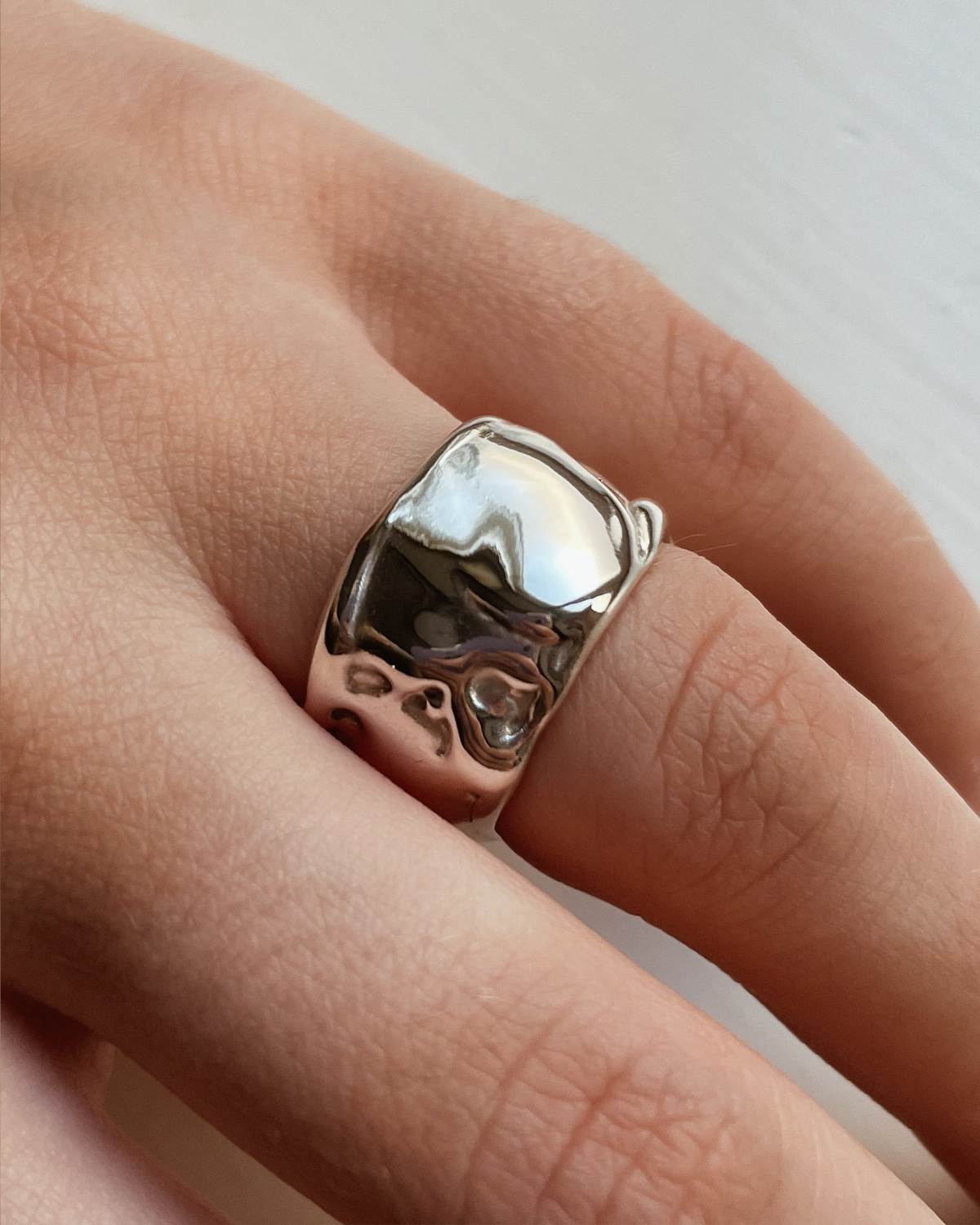 Silver ring with a unique design on a finger against a neutral background