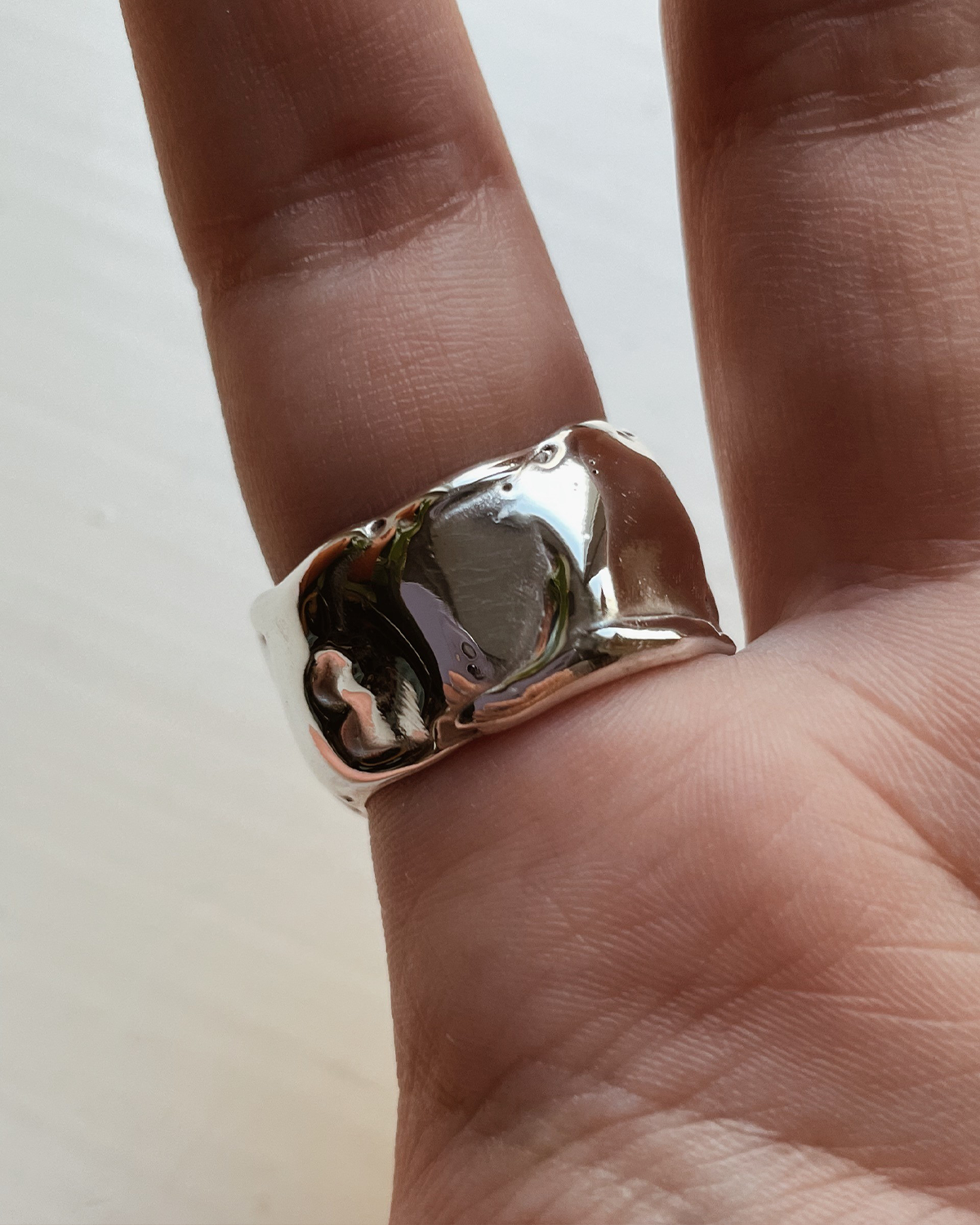 Silver ring on a finger against a neutral background