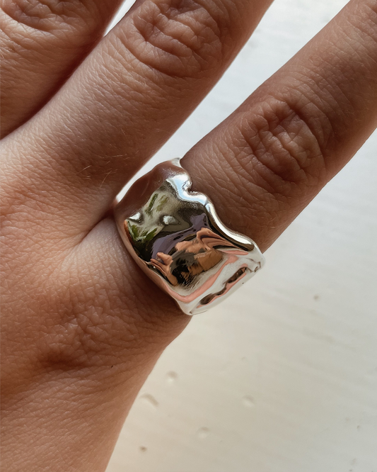 Silver ring on a finger against a neutral background