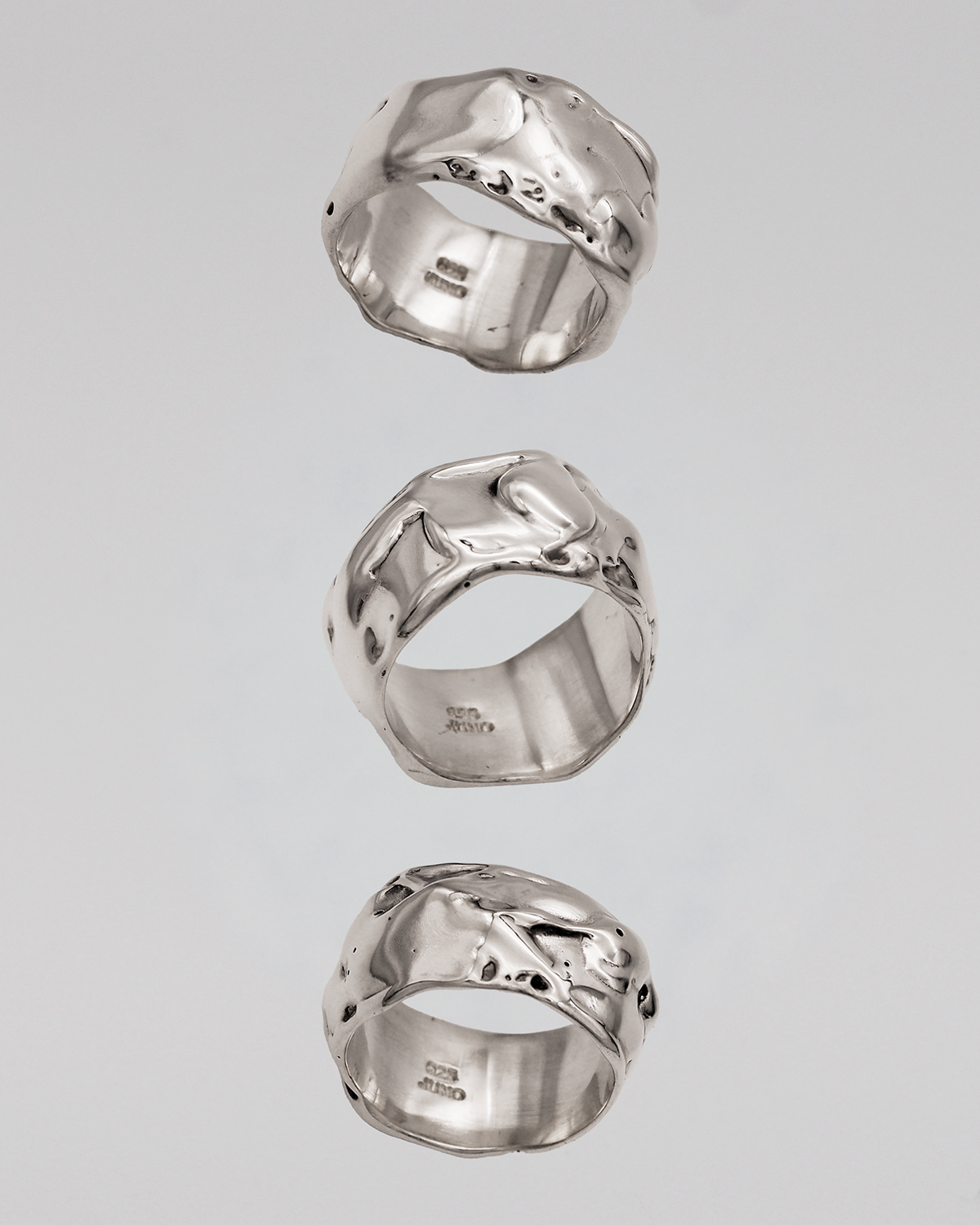 Three silver rings with unique designs on a gray background
