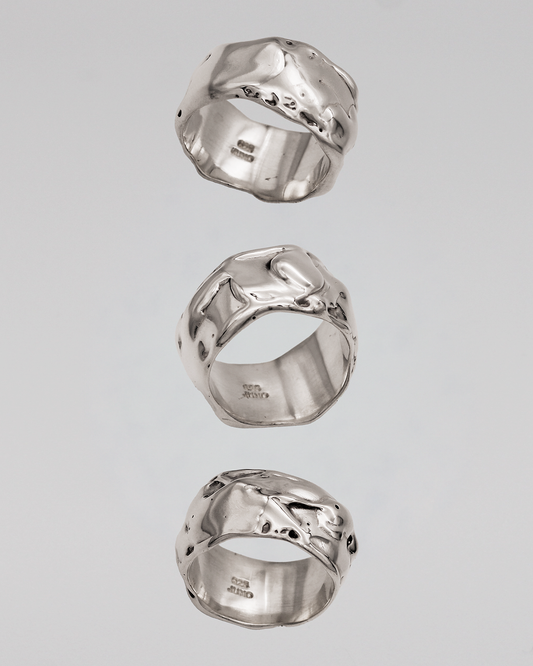 Three silver rings with unique designs on a gray background