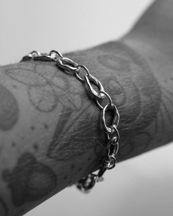 Silver chain bracelet on a tattooed arm with a blurred background